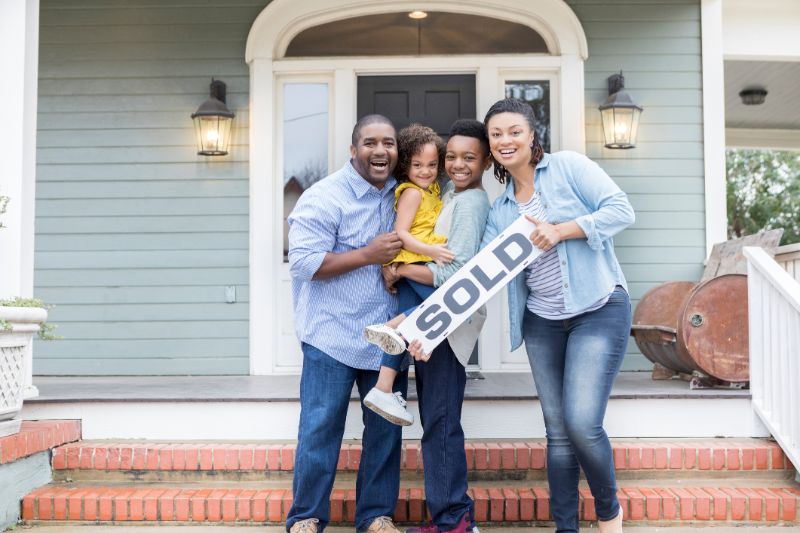 Happy family posting in front of newly bought home while holding the SOLD sign