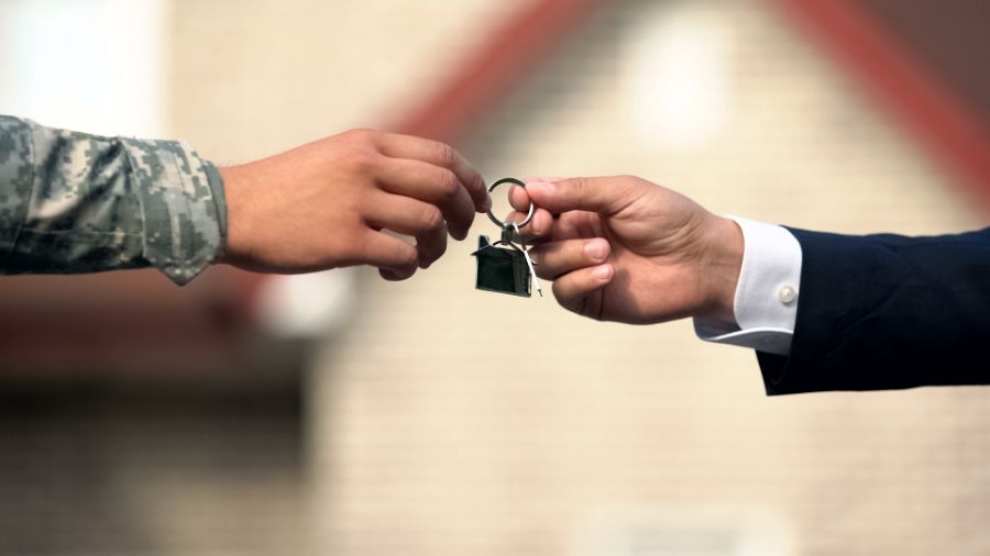 man in business suit giving house key to man in military uniform
