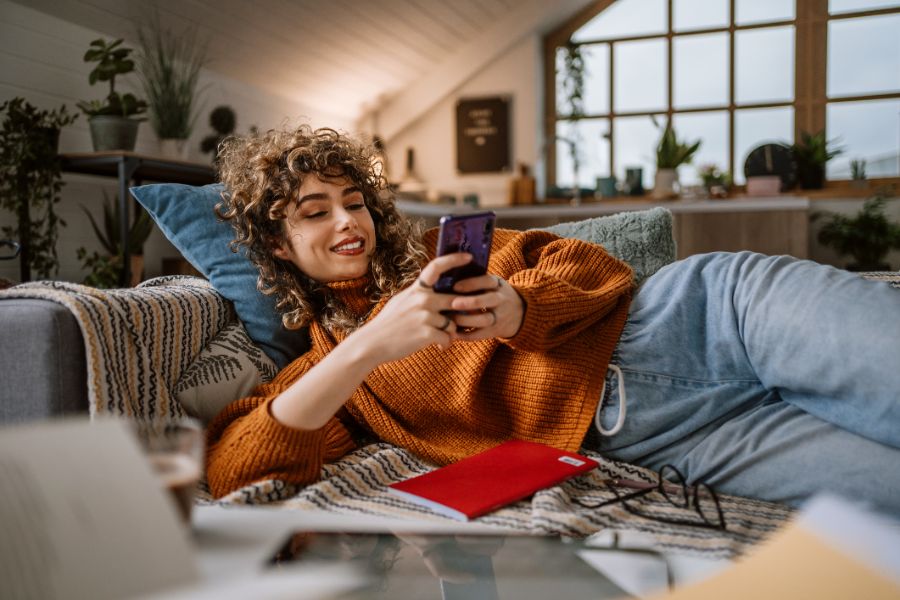 woman using smart phone for social media laying in her couch