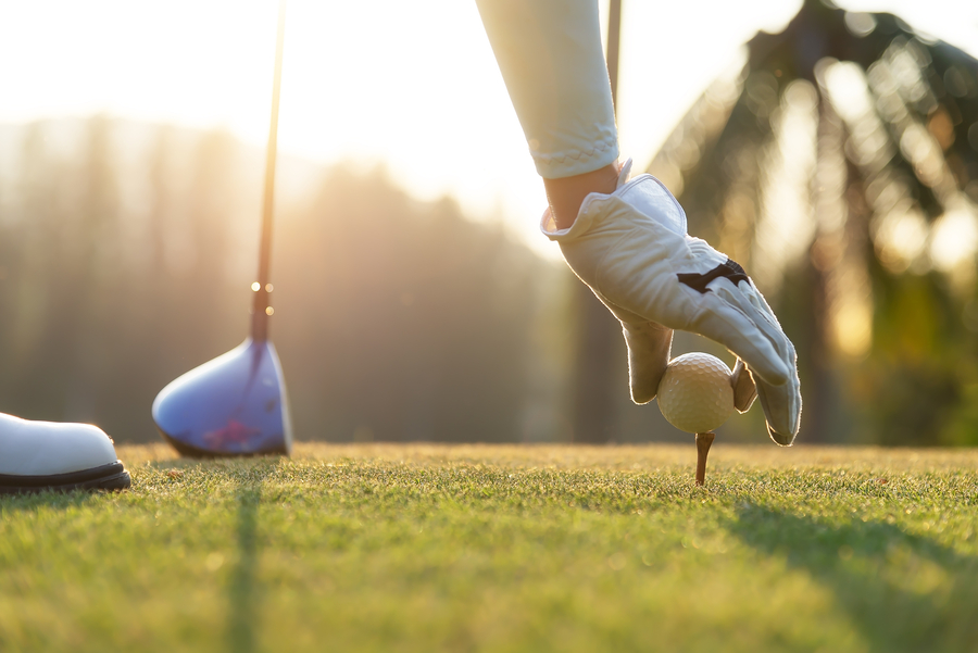 hand of woman golf player gentle put a golf ball onto wooden tee on the tee off, to make ready hit away from tee off to the fairway ahead.
