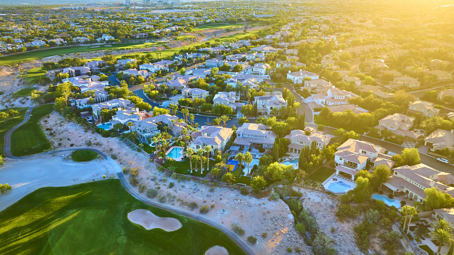 Golden hour over a luxurious Las Vegas suburb, showcasing elegant homes with pools and a golf course